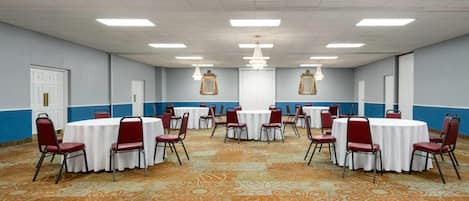 Una sala de conferencias con varias mesas redondas, sillas rojas y una alfombra estampada.