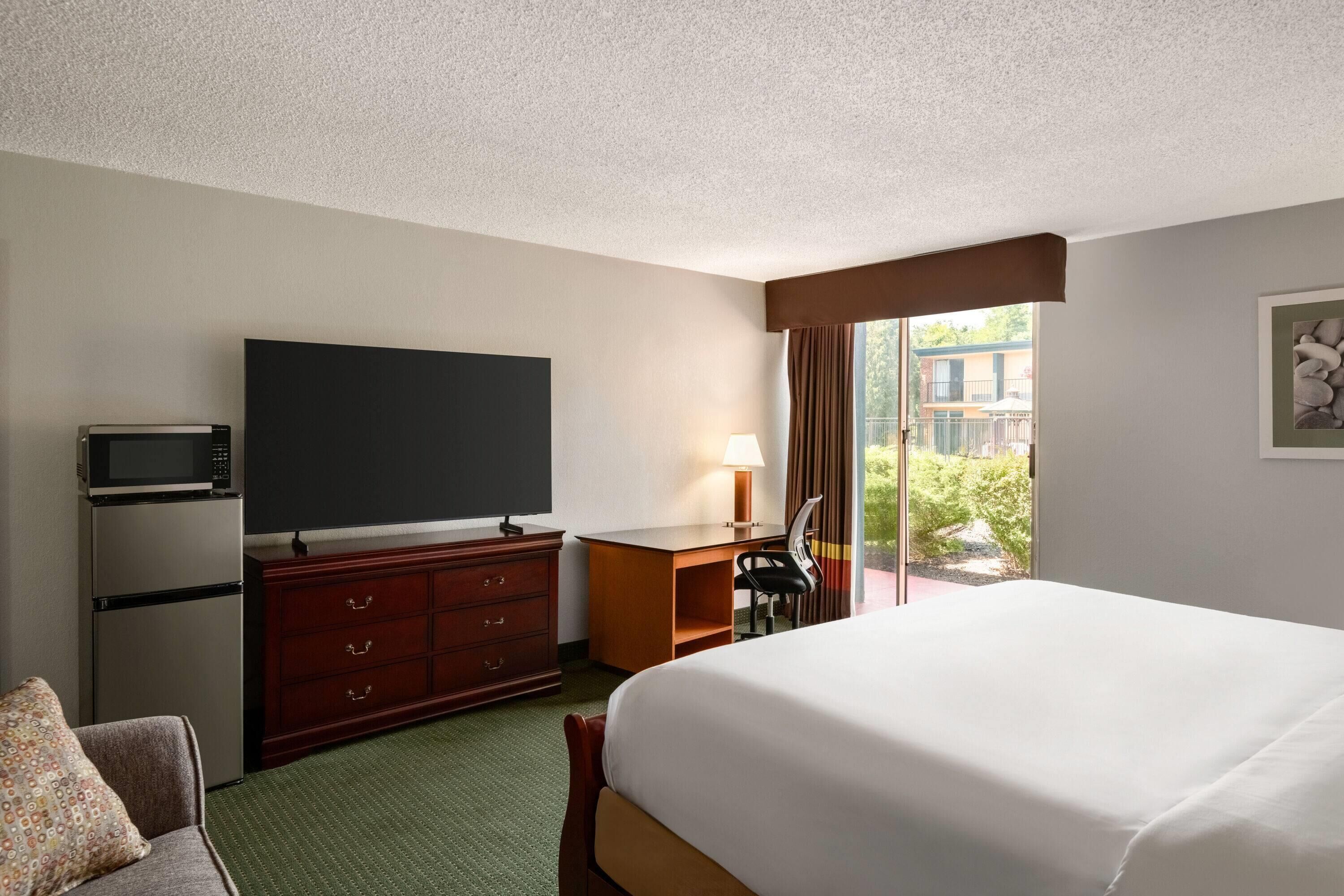 A hotel room with a bed, a desk, a television, a microwave, and a dresser.