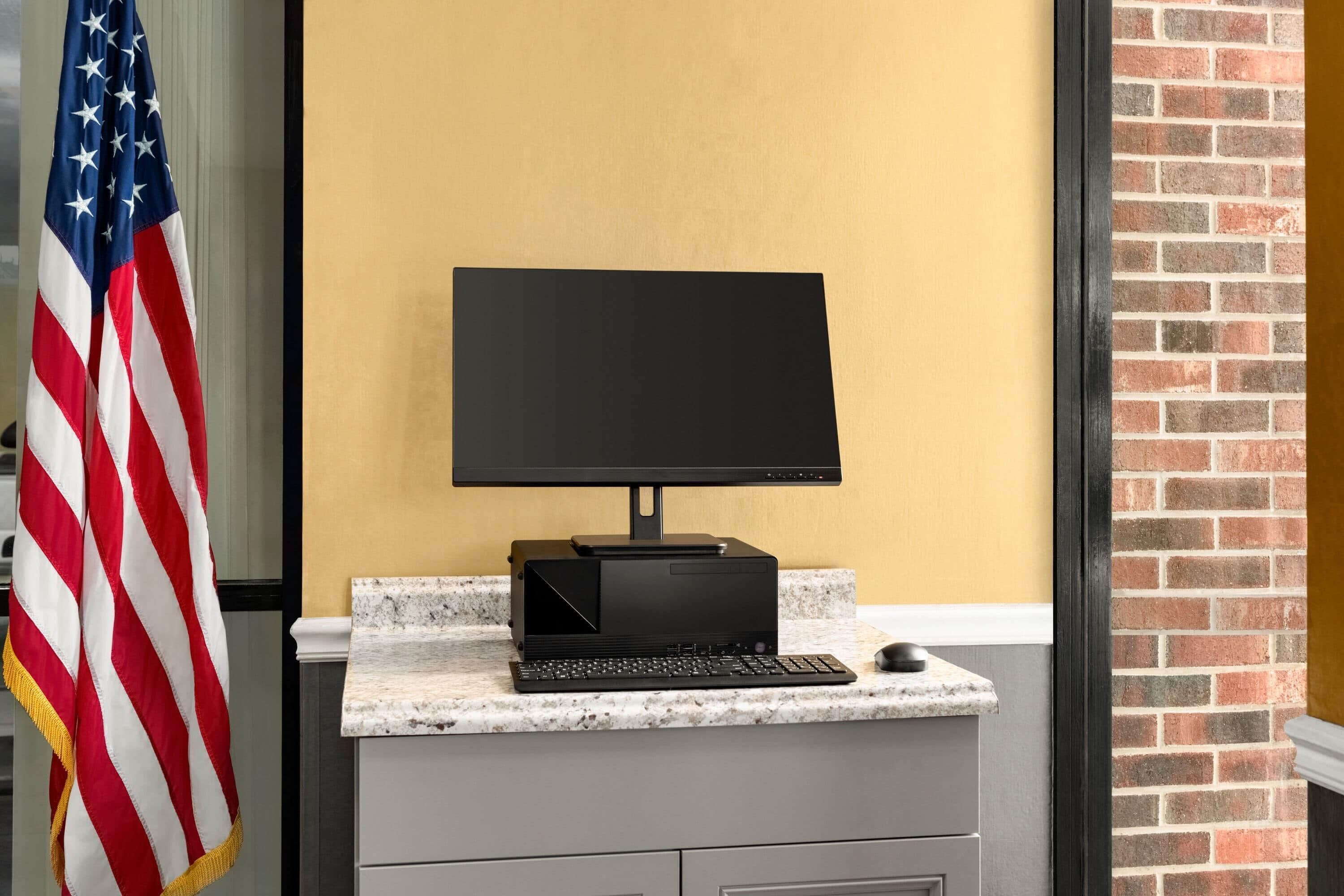 A computer setup on a granite countertop with a monitor, keyboard, and mouse.