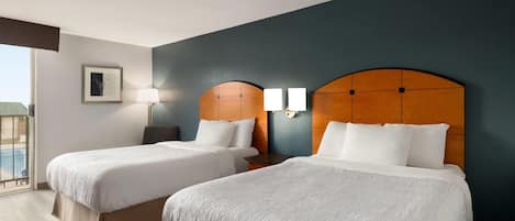 A hotel room with two beds, a view of the pool, and a framed picture on the wall.