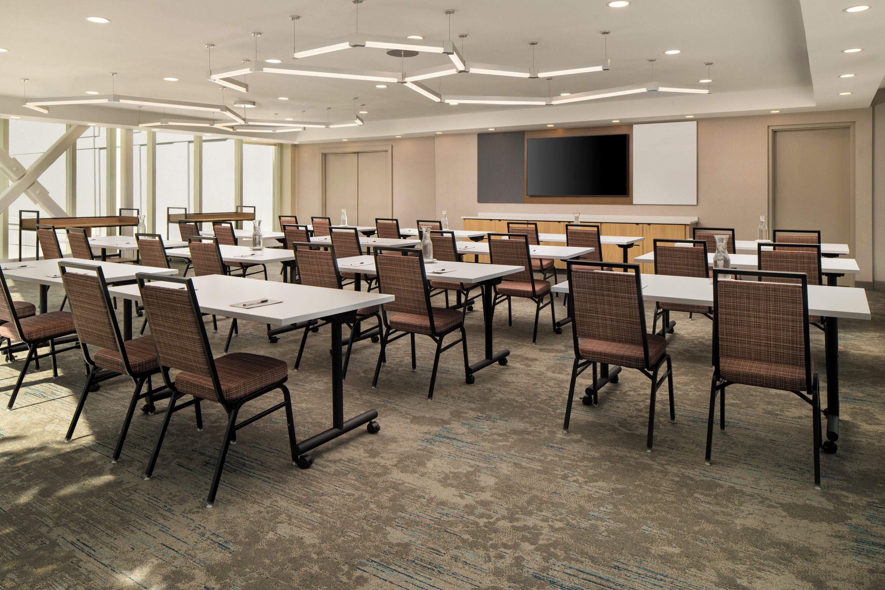 A conference room with tables and chairs, a large screen, and a carpeted floor.