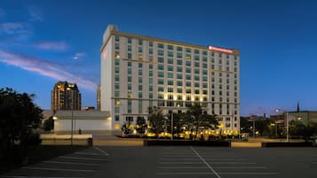 Hotel de diversos pisos amb un ampli pàrquing al davant, cel blau i un edifici a la distància.