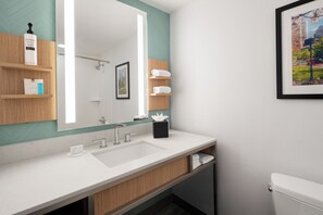 A modern bathroom with a large mirror, a white sink, and a toilet. There are wooden shelves with toiletries and a framed picture on the wall.