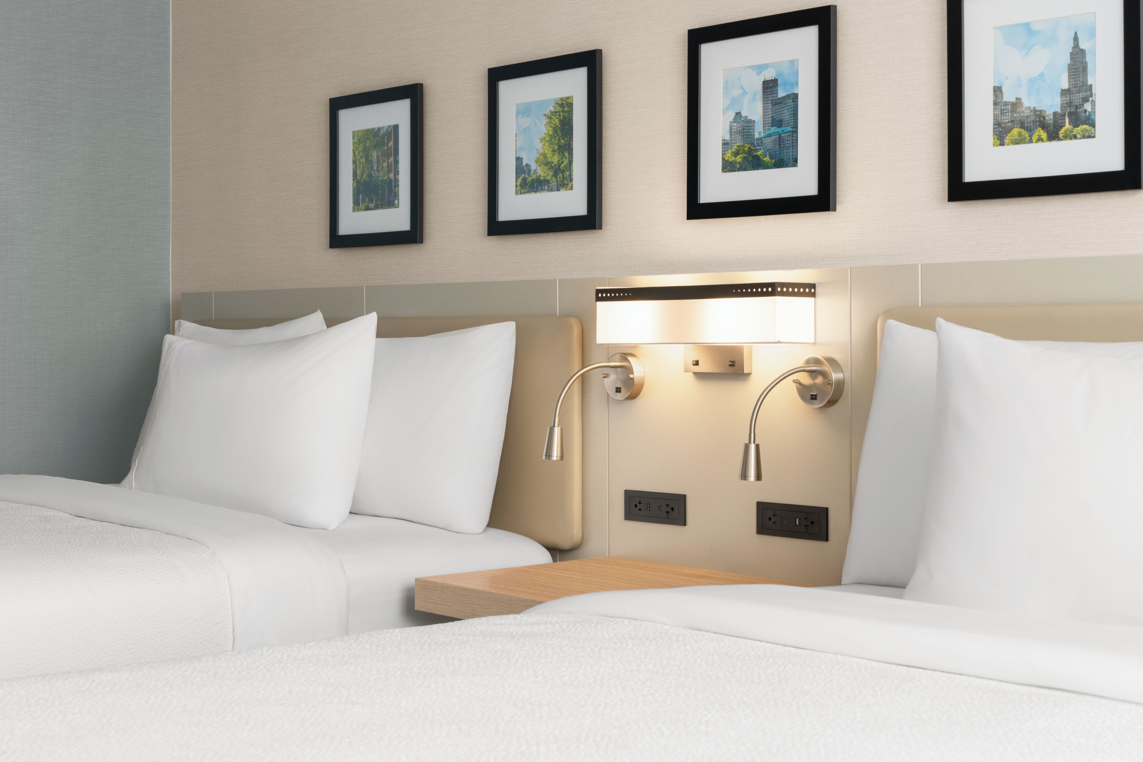 A hotel room with two beds, a bedside table, and wall-mounted lighting.