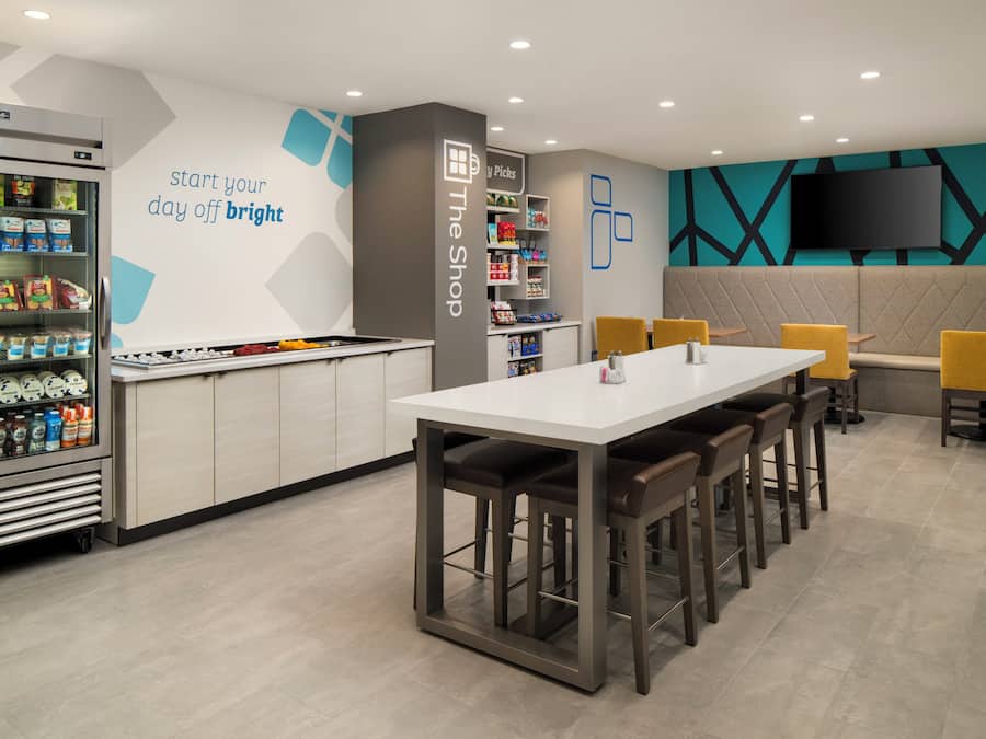 A modern cafe with a white counter, seating area, and a beverage fridge.