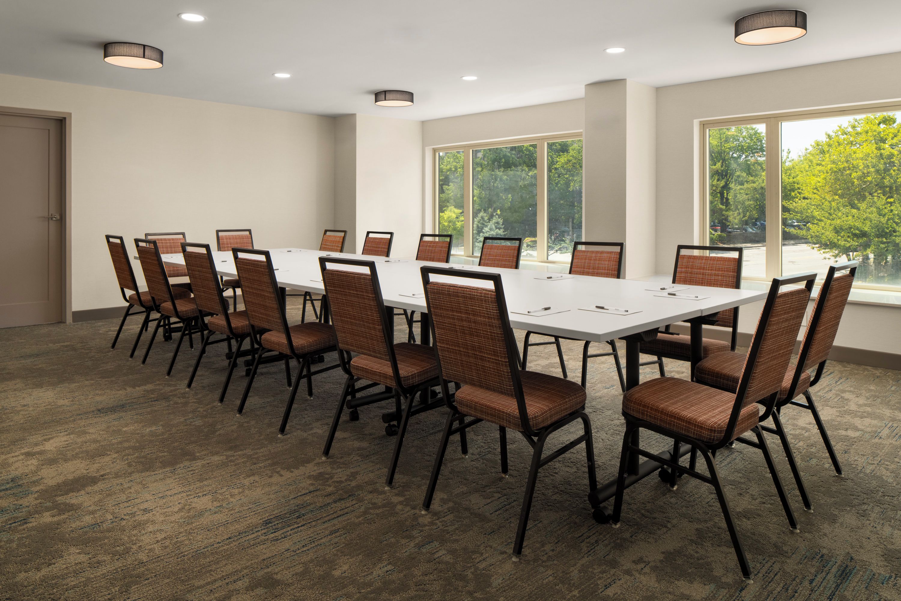 Un salón de conferencias con una mesa larga y sillas, ventanas grandes y luces en el techo.