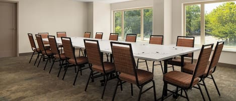 A conference room with a long table and chairs, large windows, and ceiling lights.