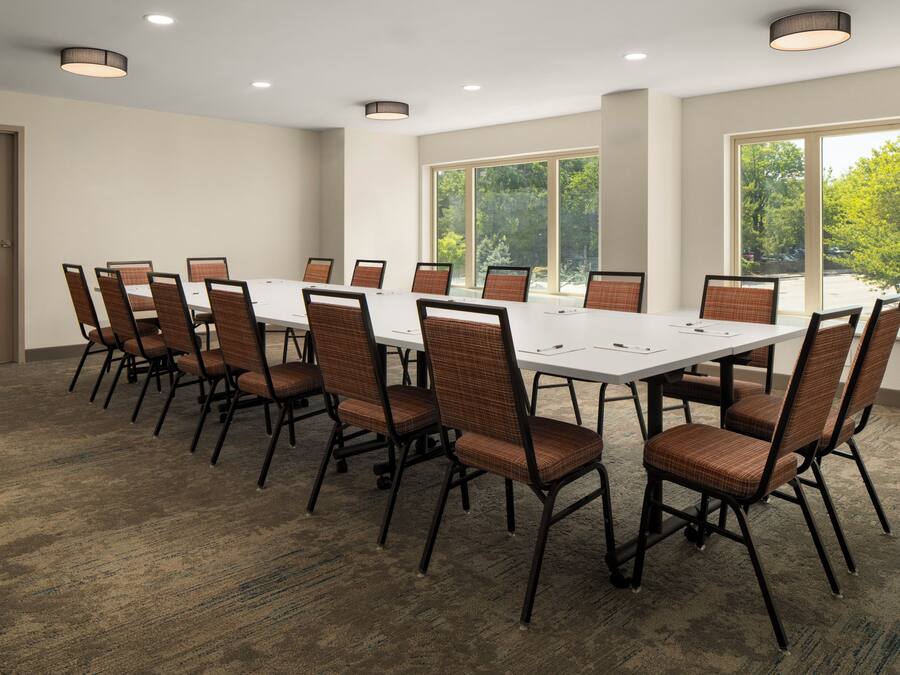 Un salón de conferencias con una mesa larga y sillas, ventanas grandes y luces en el techo.