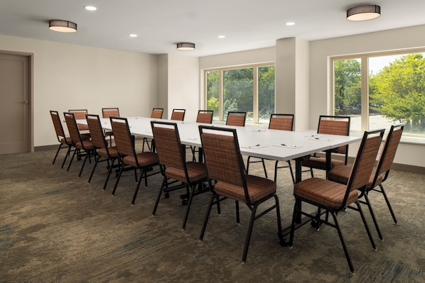 Un salón de conferencias con una mesa larga y sillas, ventanas grandes y luces en el techo.