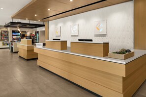 A hotel reception area with a modern design, featuring a wooden reception desk, a digital display, and a wall-mounted artwork. - Hilton Garden Inn Providence Downtown Convention Center (Providence)