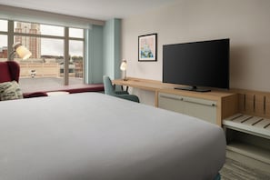 Habitación de hotel con una cama grande, un escritorio, un televisor de pantalla plana, una silla, una lámpara y una ventana con vista a la ciudad.