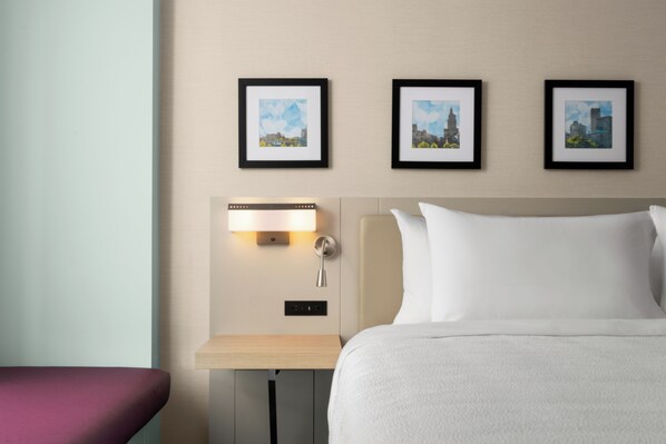 Une chambre d’hôtel avec un lit, une table de chevet avec une lampe et trois tableaux encadrés accrochés au mur.