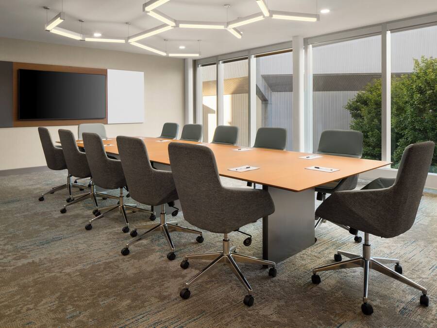 Une salle de conférence avec une longue table, de nombreuses chaises, un téléviseur à écran plat et de grandes fenêtres.