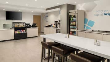 Un café moderno con una barra alargada, taburetes, una máquina de café y un refrigerador lleno de bebidas.