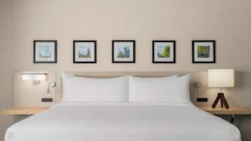 Ein Hotelzimmer mit einem großen Bett, einem Nachttisch mit Lampe und fünf gerahmten Bildern an der Wand.