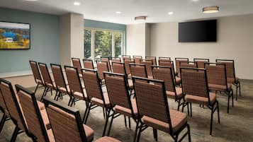 A conference room with rows of chairs, a flat-screen TV on the wall, and a window with a view of trees.