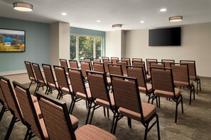 A conference room with rows of chairs, a flat-screen TV on the wall, and a window with a view of trees. - Hilton Garden Inn Providence Downtown Convention Center (Providence)