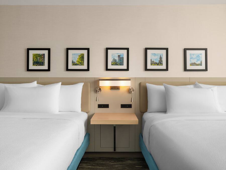 A hotel room with two beds, a nightstand, and a wall-mounted light.