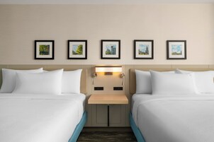 Habitación de hotel con dos camas, una mesita de noche y una lámpara en la pared.