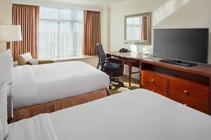 A hotel room with two beds, a desk, a chair, a television, and a large window with curtains.