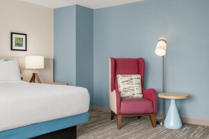 Una habitación de hotel con cama, una silla, una mesita y una lámpara de pie.