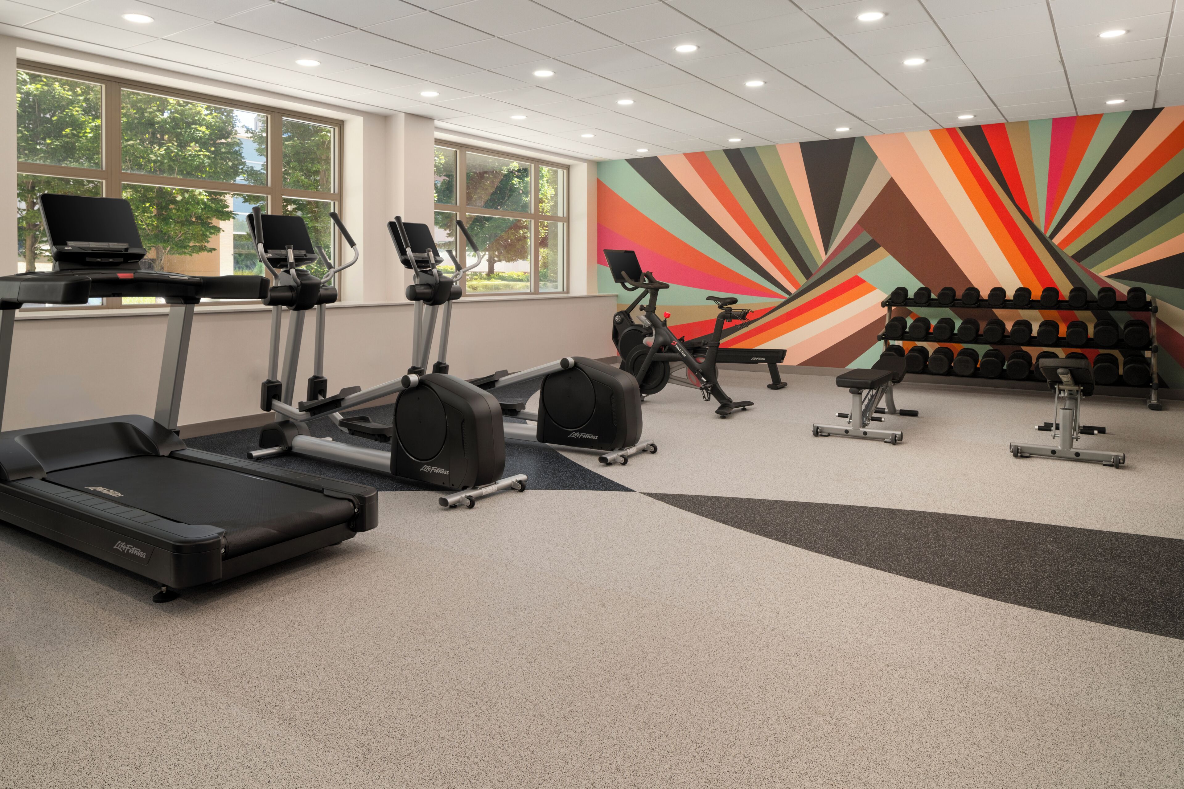 A gym with treadmills, stationary bikes, and a wall of colorful geometric patterns.