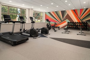 Un gimnasio con cintas de correr, bicicletas estáticas y una pared de patrones geométricos coloridos.
