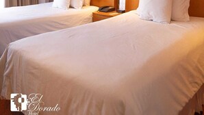Una habitación de hotel con dos camas, una mesita de noche con teléfono y una ventana con cortinas.