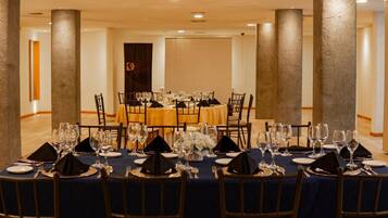 A conference room with round tables set for a formal event, featuring dark blue tablecloths, black napkins, and glassware.