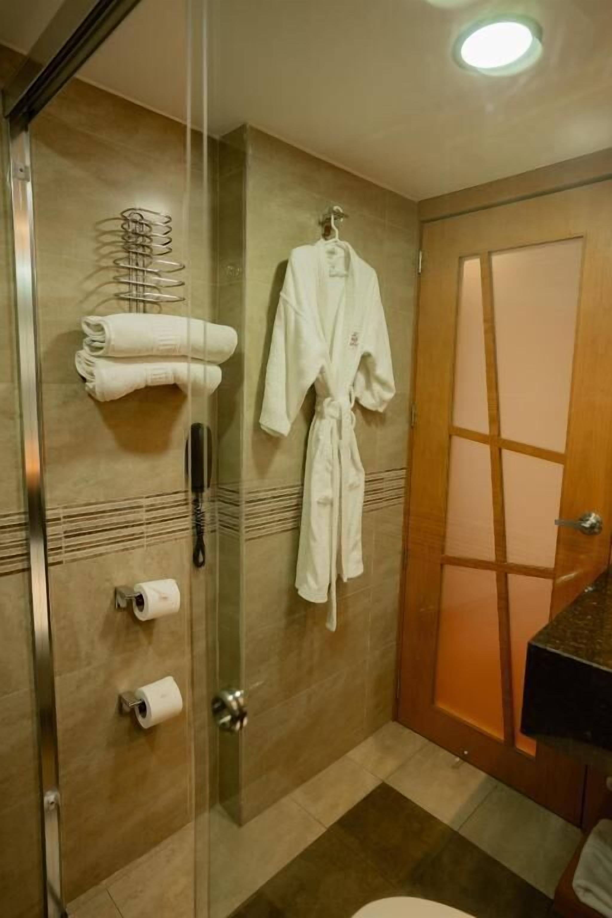 A bathroom with a glass shower enclosure, a wooden door, and a towel rack with folded towels.