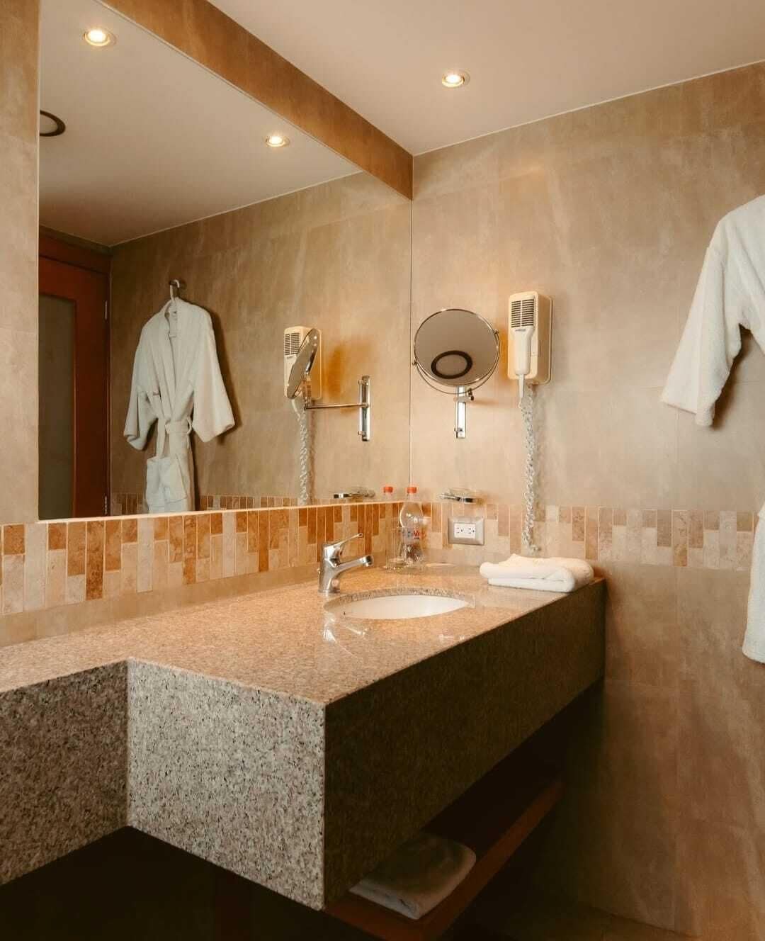 Un baño moderno con encimera de granito, lavamanos, espejo y perchero.