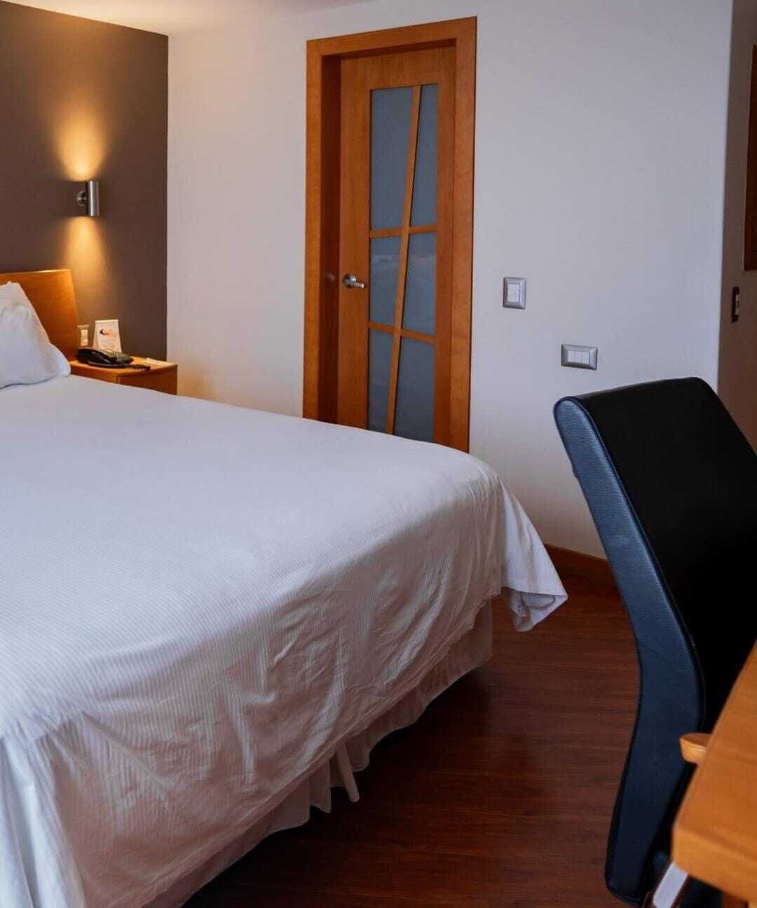 Una habitación de hotel con una cama, una puerta de madera, un escritorio y una silla.