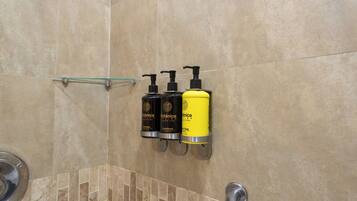 Baño con tres artículos de tocador colgados en la pared, una repisa de vidrio y una zona de ducha.