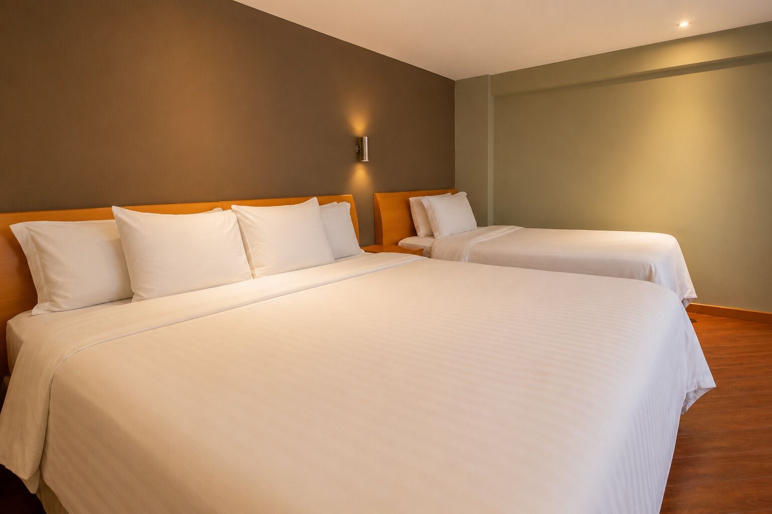 A hotel room with two beds, a wall-mounted light, and a wooden floor.