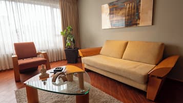Una sala de estar con un sofá, sillones, una mesa de centro de vidrio, una planta en maceta y un cuadro en la pared.