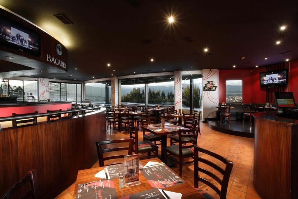 Un restaurante con barra, mesas, sillas y vistas a las montañas.