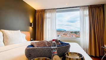 Habitación de hotel con una cama grande, vistas a un paisaje urbano y dos cuencos para mascotas sobre la cama.