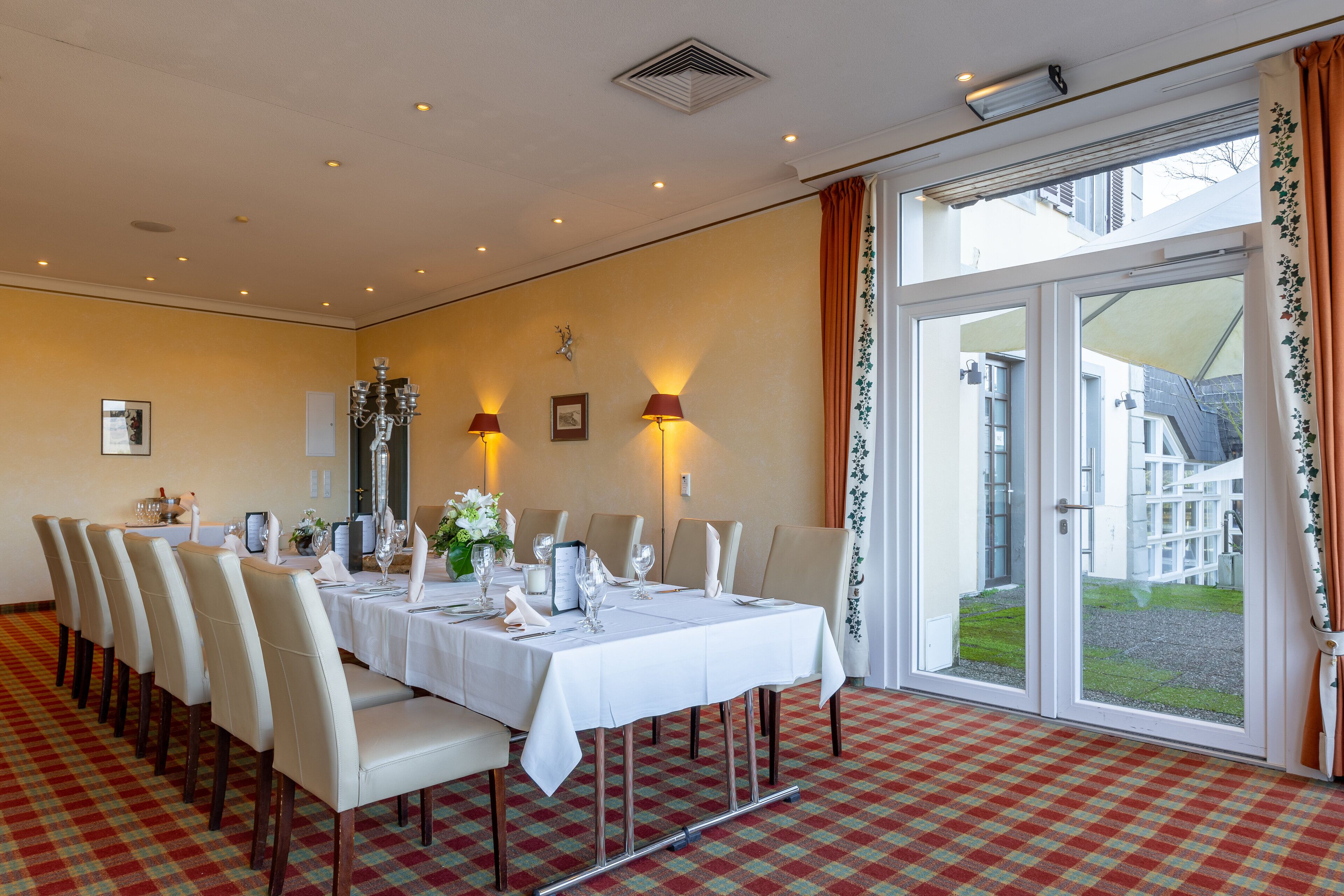 A dining room with a checkered floor, a long table set for a meal, and a view through a glass door.
