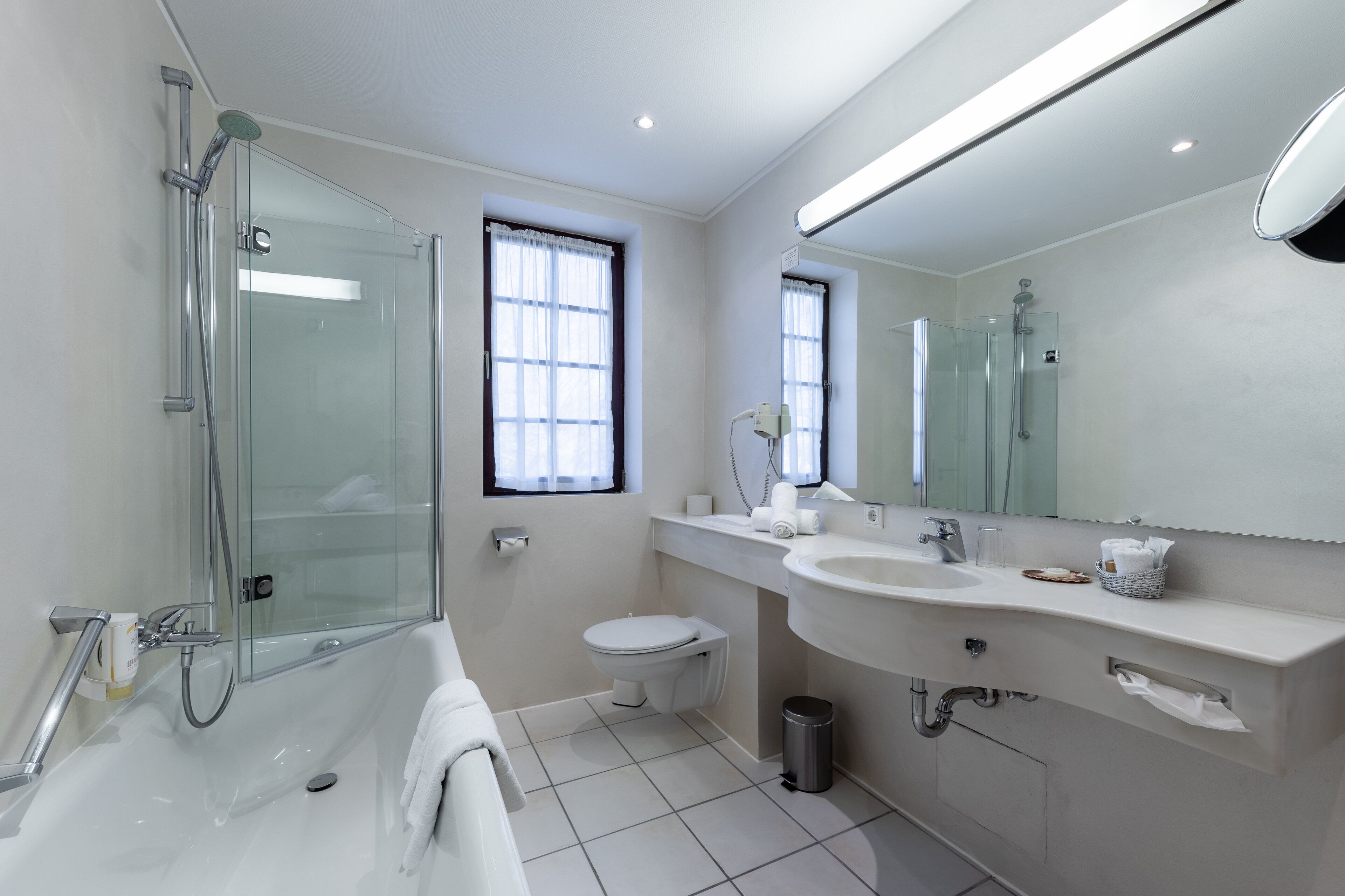 Ein modernes Badezimmer mit einer Duschkabine, einer Toilette, einem Waschbecken mit Spiegel und einem Fenster.
