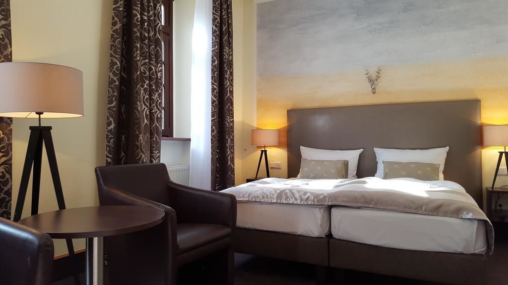 Une chambre d’hôtel avec un lit, deux lampes de chevet, une chaise, une petite table et des rideaux à motifs.