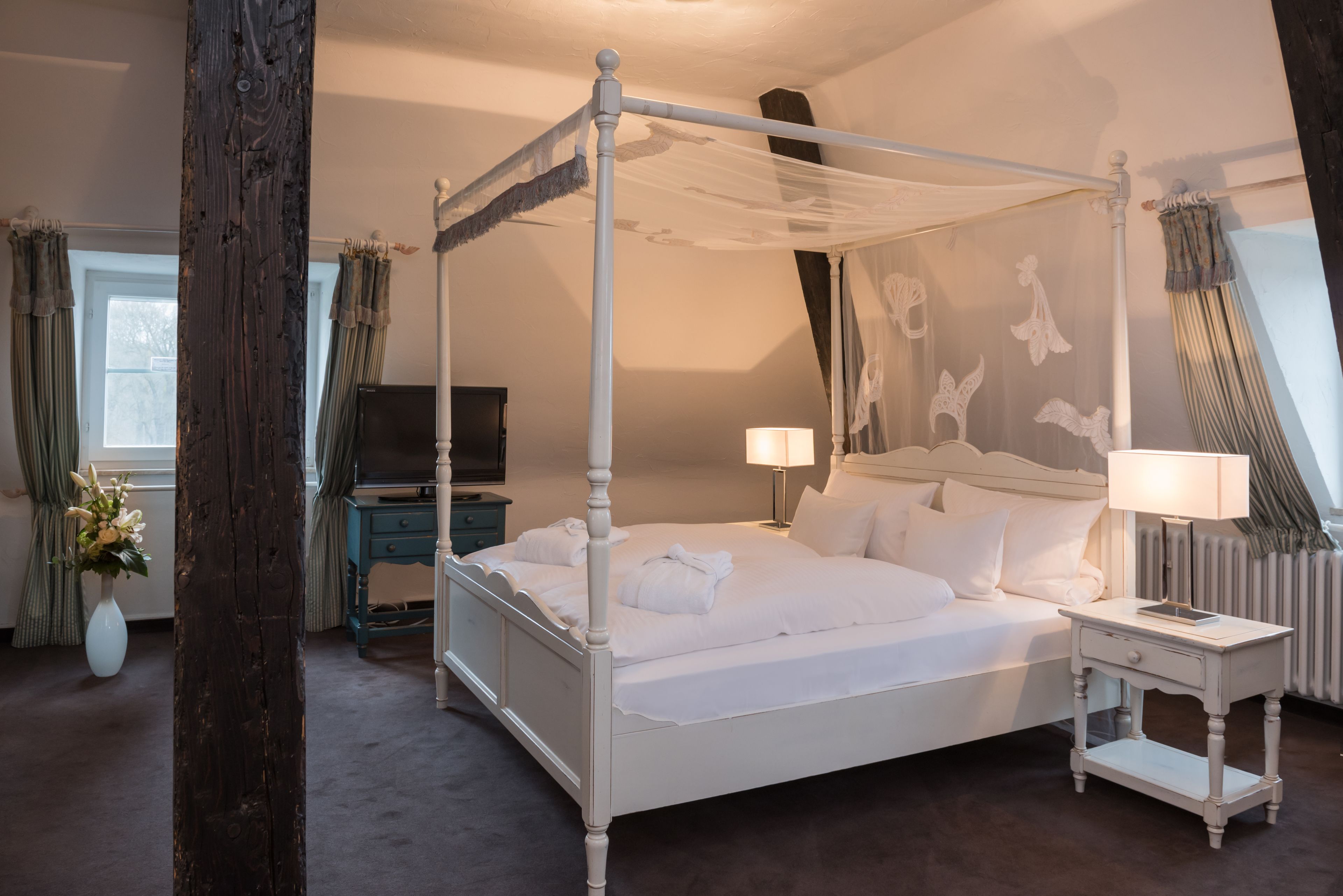 Ein Hotelzimmer mit einem Himmelbett, einem Fernseher, Nachttischen und einer Blumenvase.