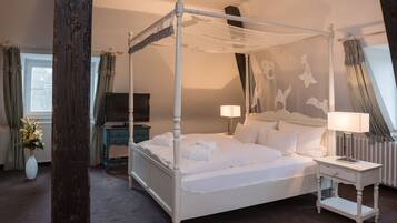 Ein Hotelzimmer mit einem Himmelbett, einem Fernseher, Nachttischen und einer Blumenvase.