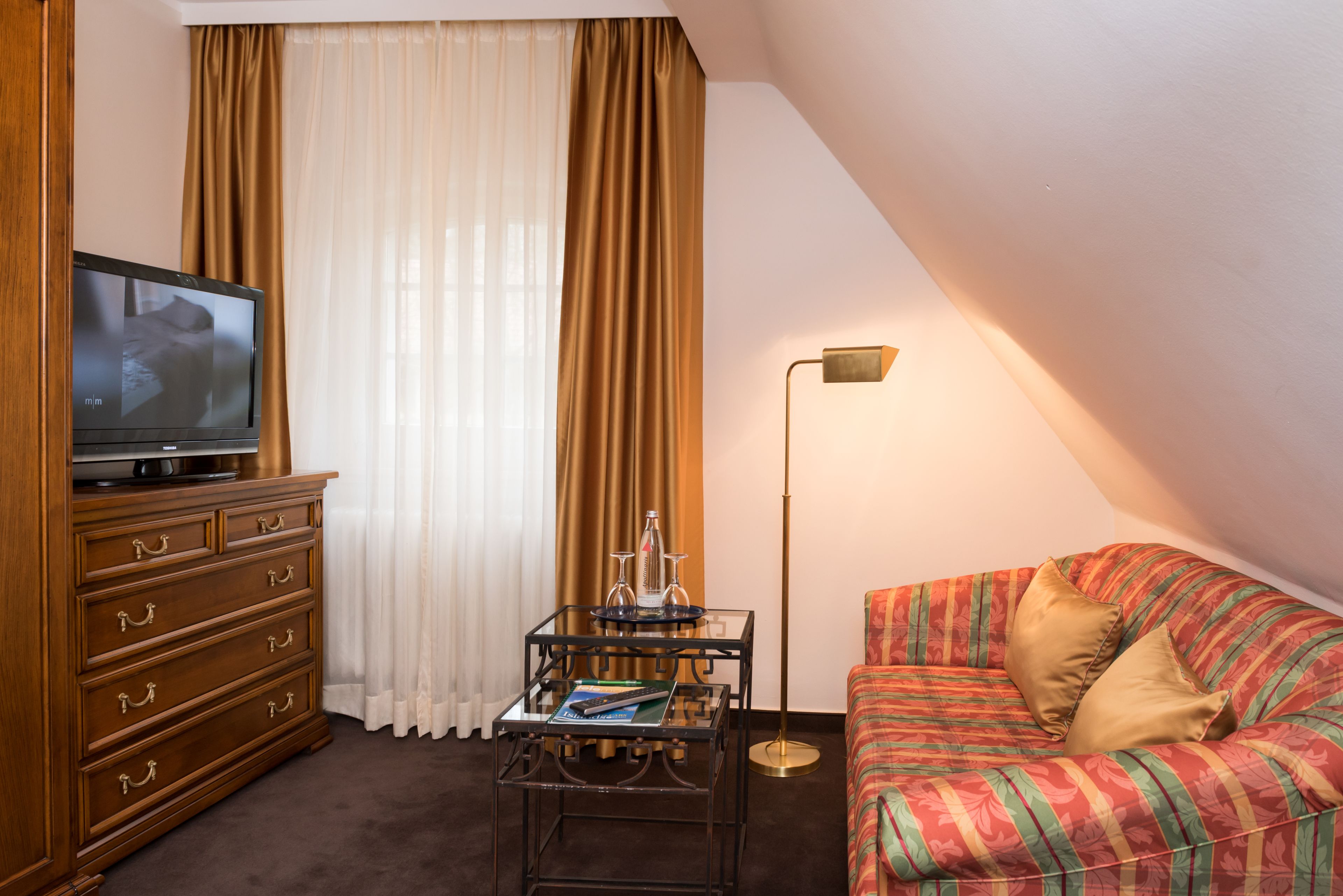 Ein gemütliches Wohnzimmer mit Fernseher, einer Holzkommode, einem Glastisch und einem farbenfrohen Sofa.
