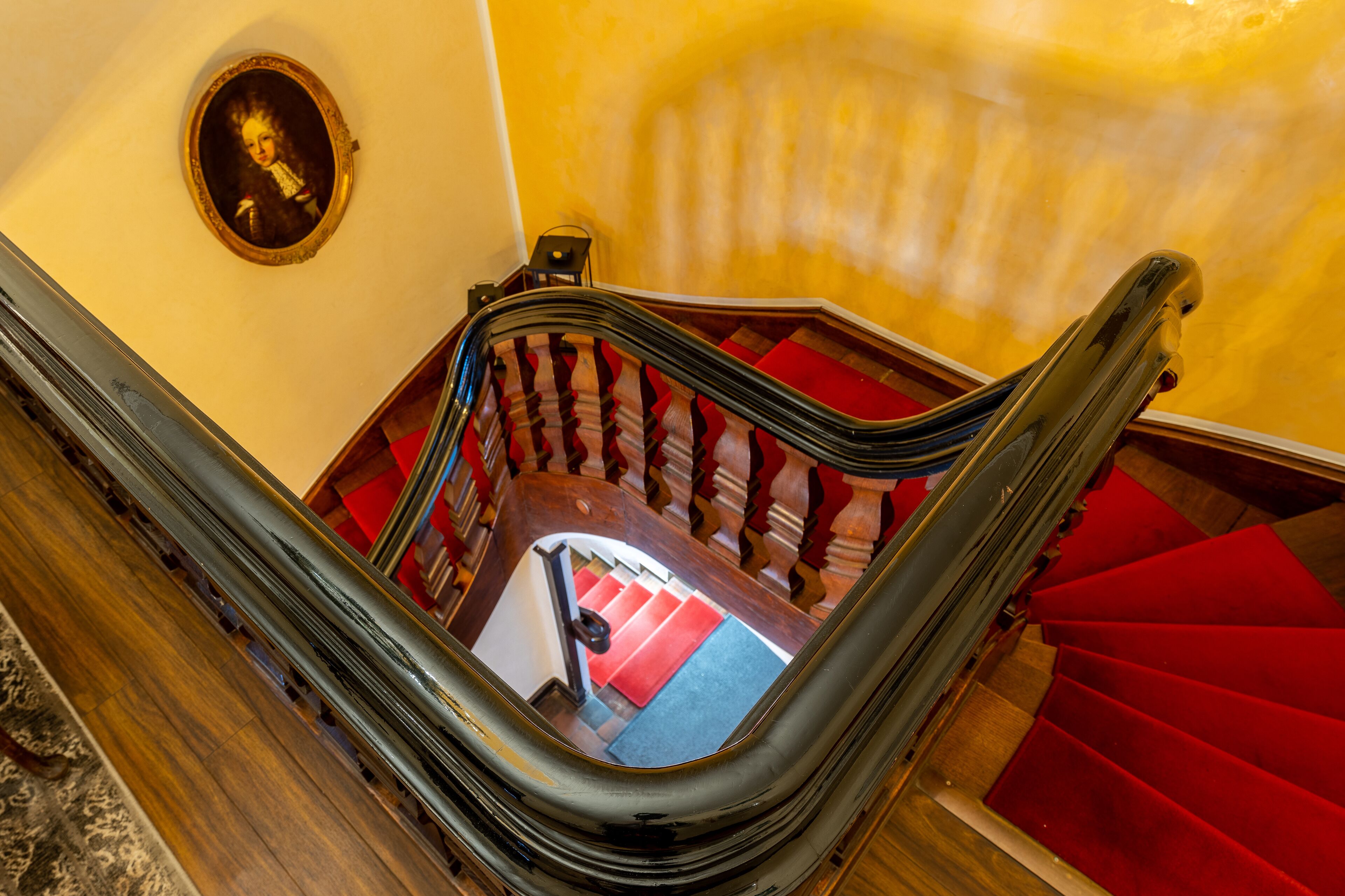 Un escalier dont les marches sont recouvertes d’une moquette rouge et qui possède une main courante en bois.