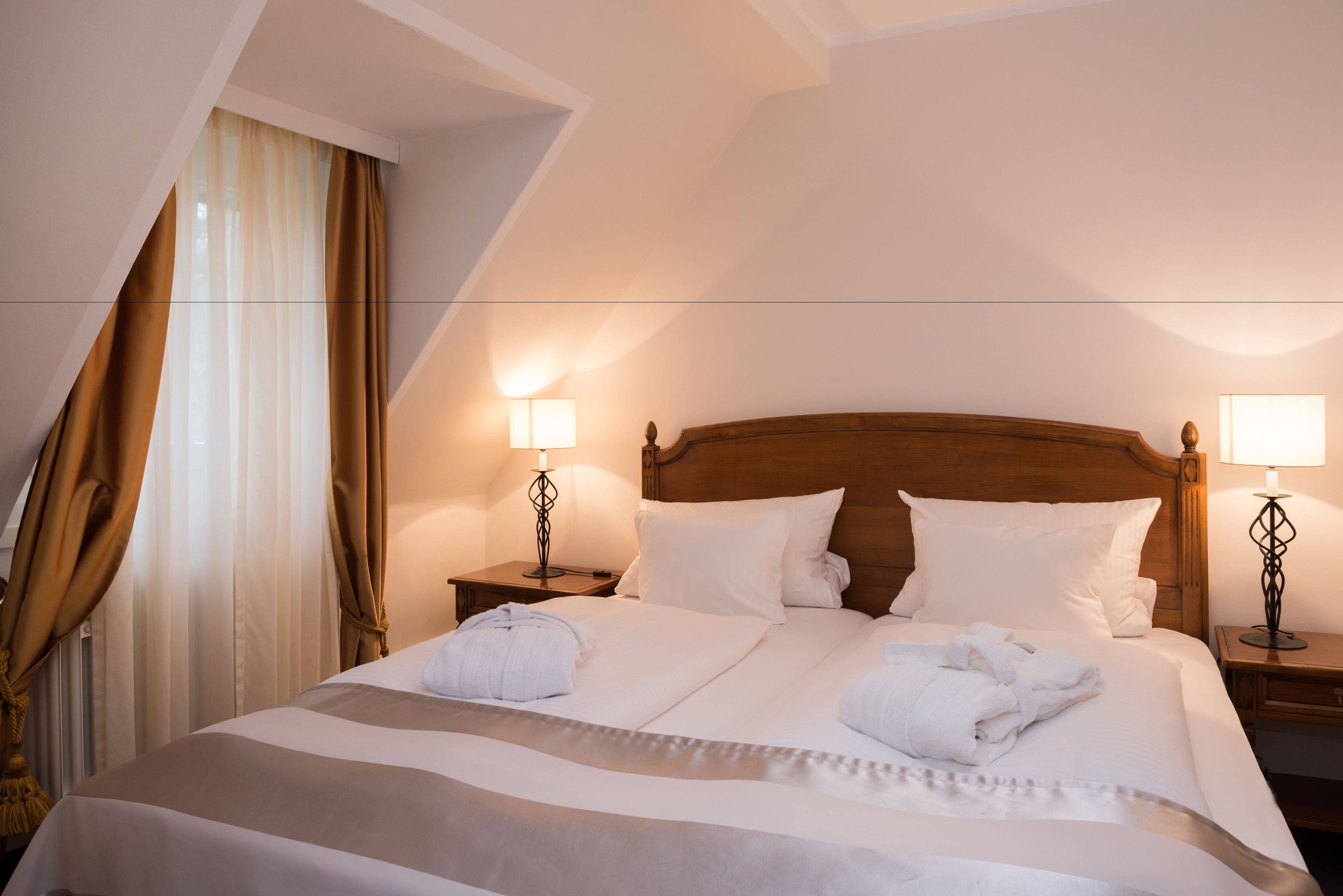 Habitación de hotel con una cama grande, dos mesitas de noche con lámparas y un ventanal con cortinas.
