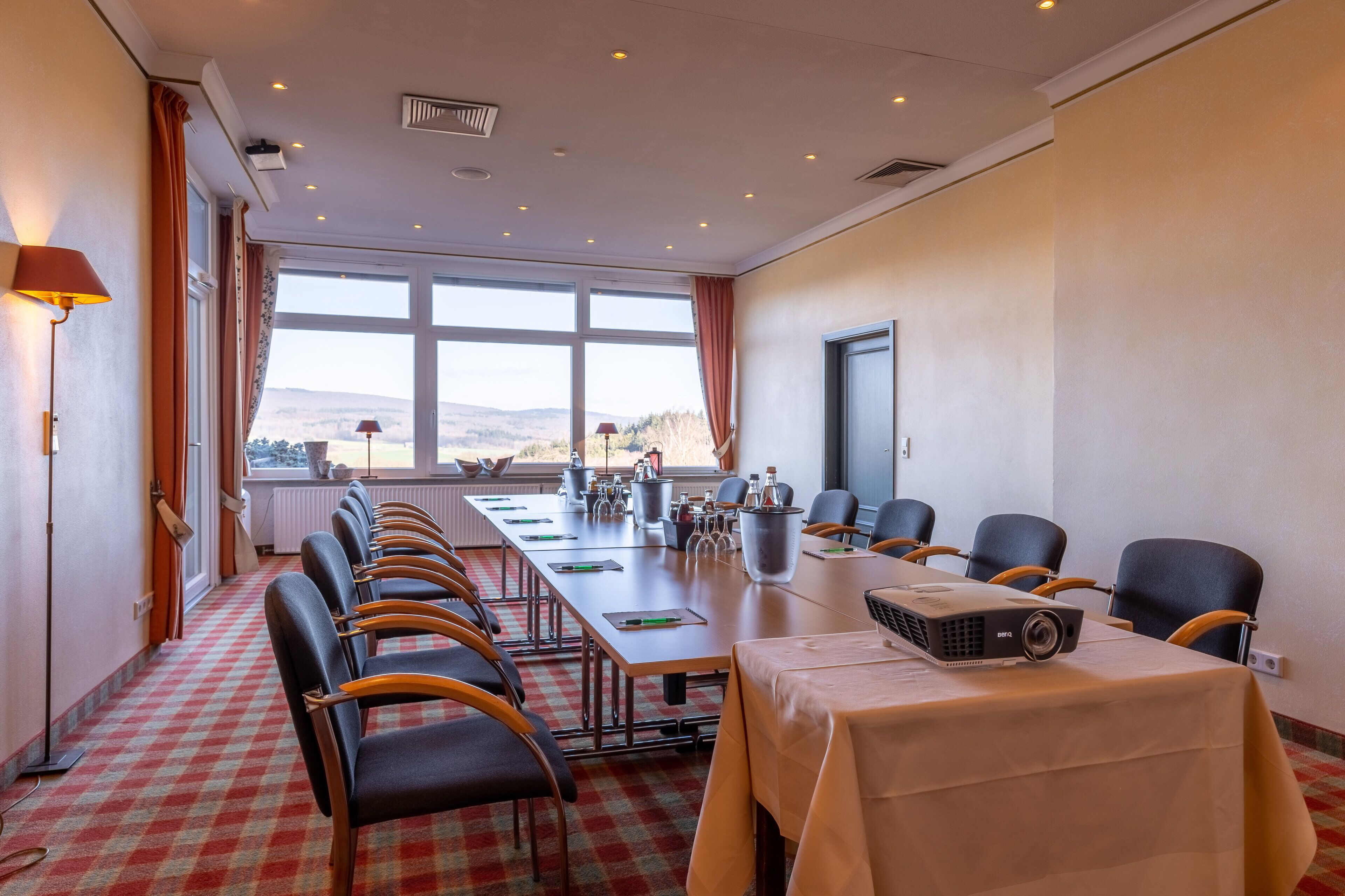 A conference room with a long table, chairs, a projector, and a view of the outdoors.