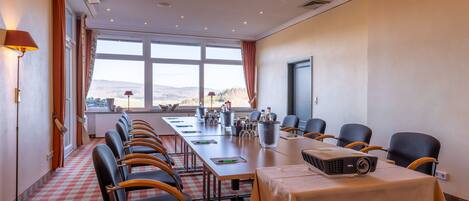 A conference room with a long table, chairs, a projector, and a view of the outdoors.