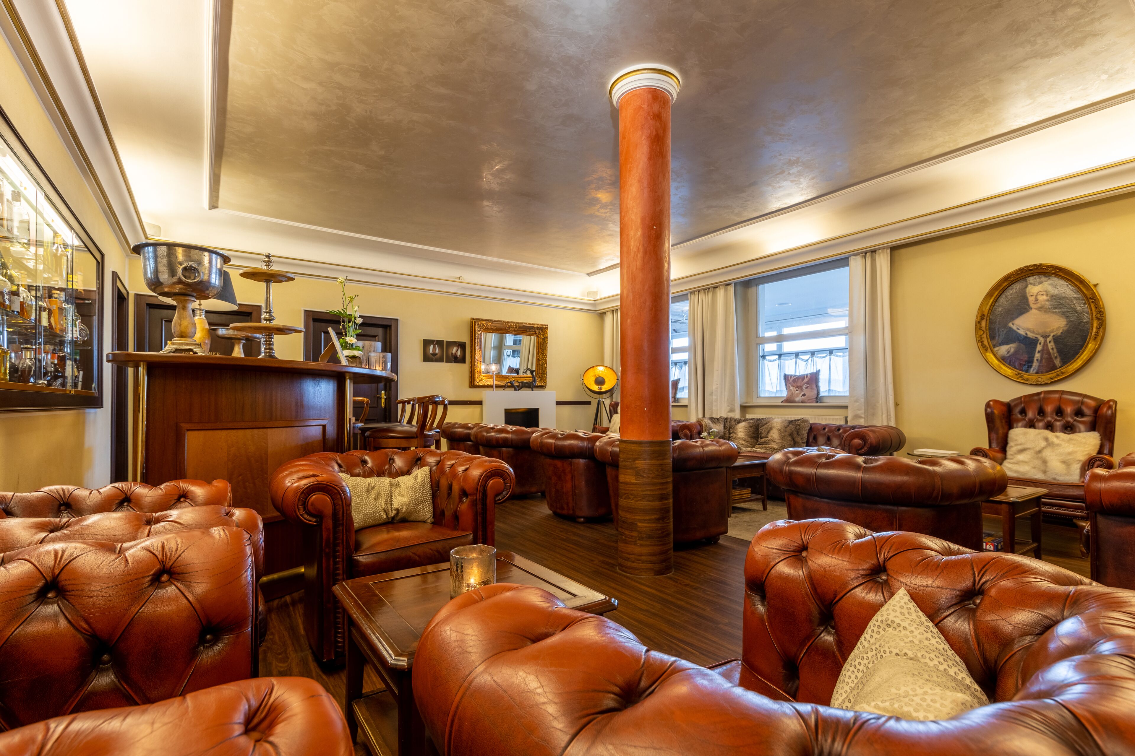 A spacious lounge with leather sofas, a central pillar, and a bar area with various items.