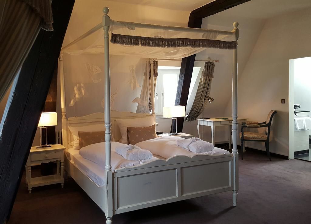 A four-poster canopy bed in a room with a sloped ceiling, a desk, and a chair.