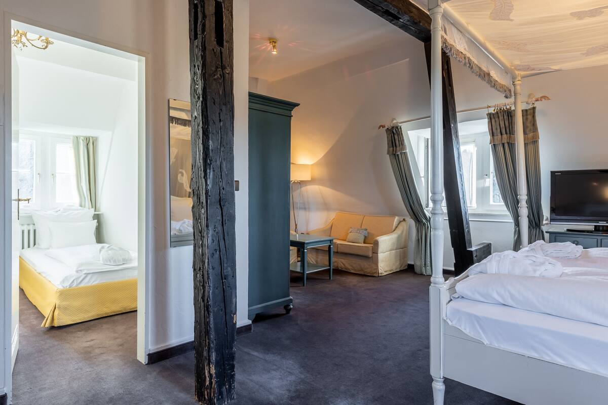 A spacious hotel room with a large bed, a sofa, a desk, and a television.